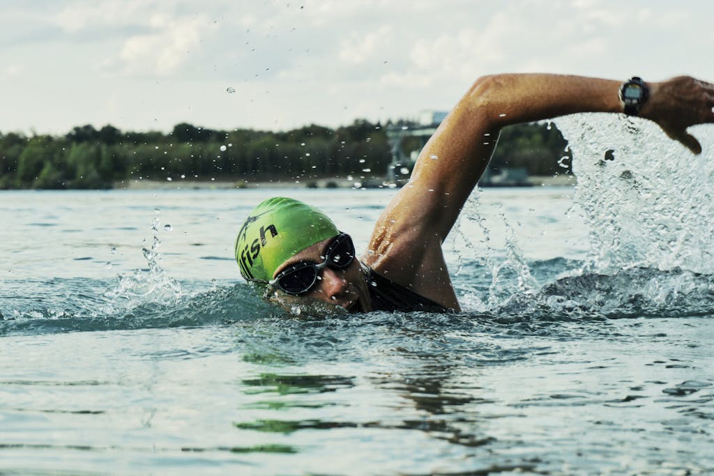 A male swimmer in a green cap and goggles competing in an open water race.