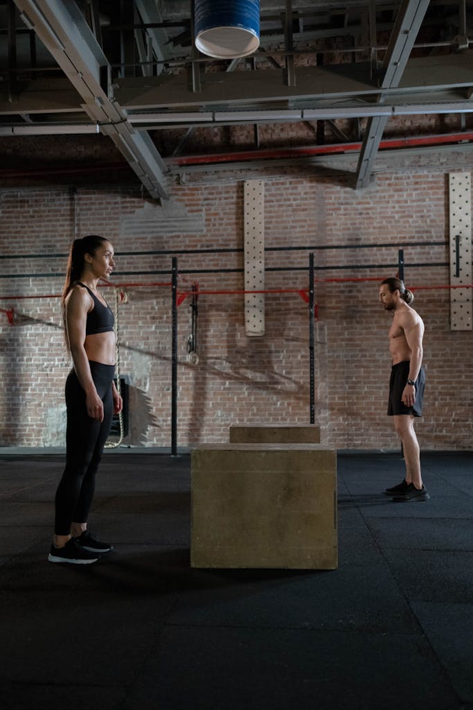 A man and woman preparing for a crossfit workout with box jumps in a spacious gym.