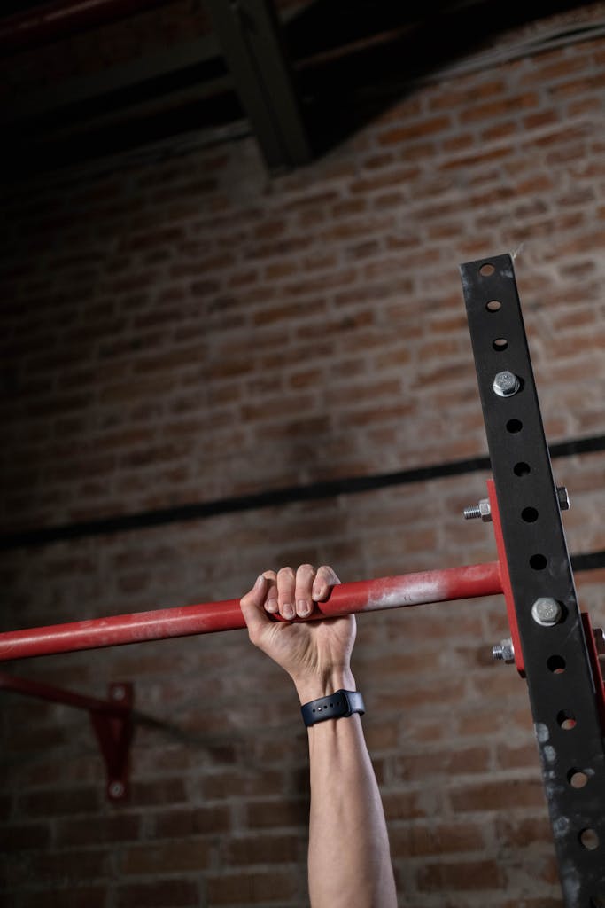 Close-up of a hand gripping a pull-up bar inside a gym with brick wall background.