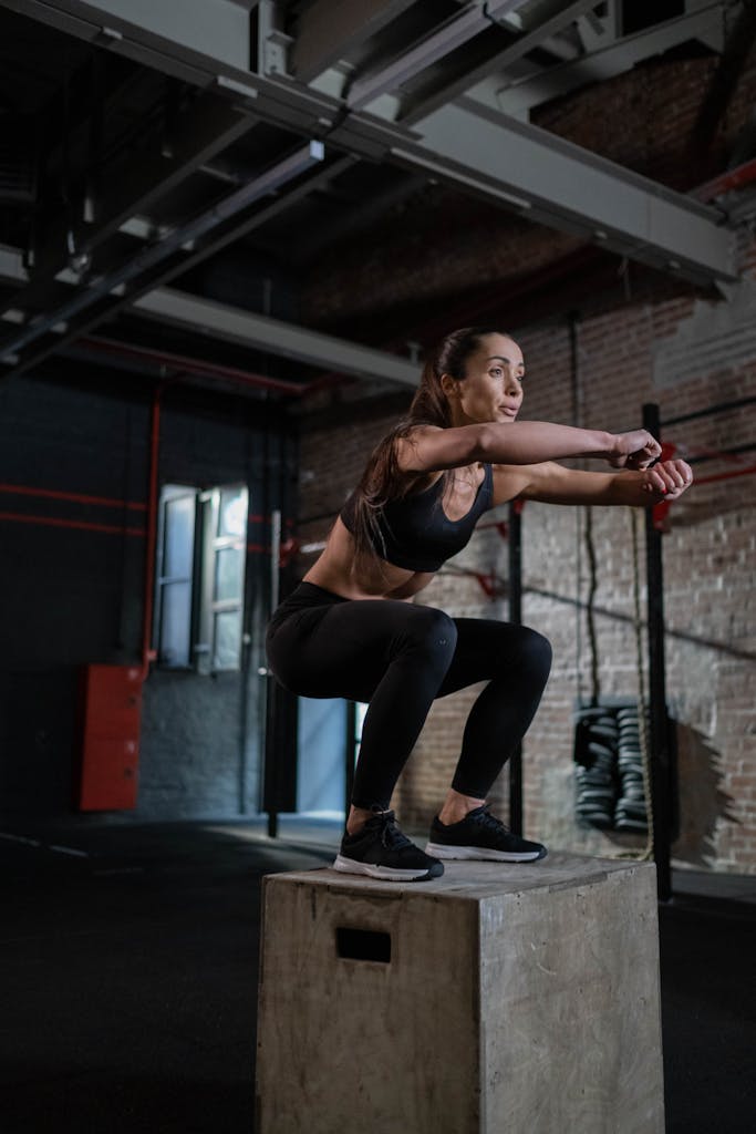 Fit woman in activewear executing a box jump inside a modern gym setting.