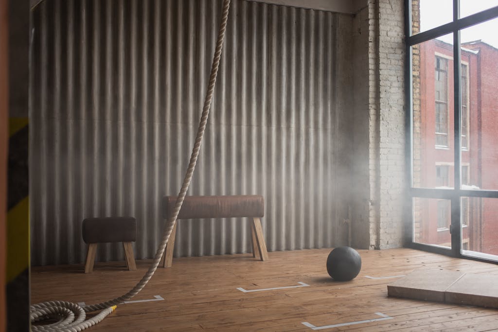Industrial-style gym interior featuring pommel horse, exercise ball, and climbing rope.