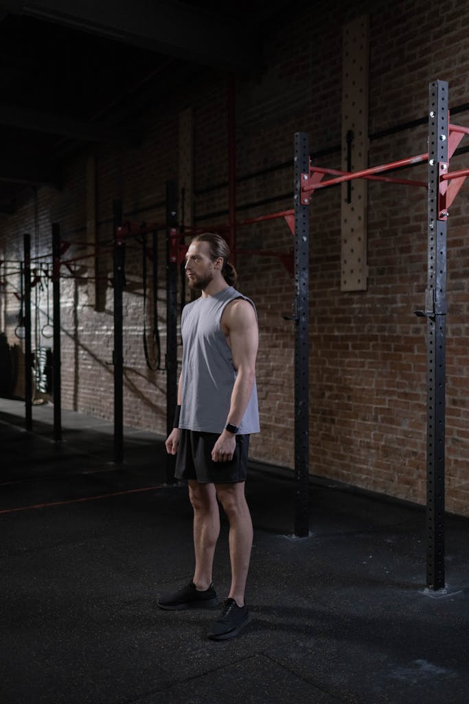 Muscular man in activewear standing in an industrial-style urban gym, looking pensive.