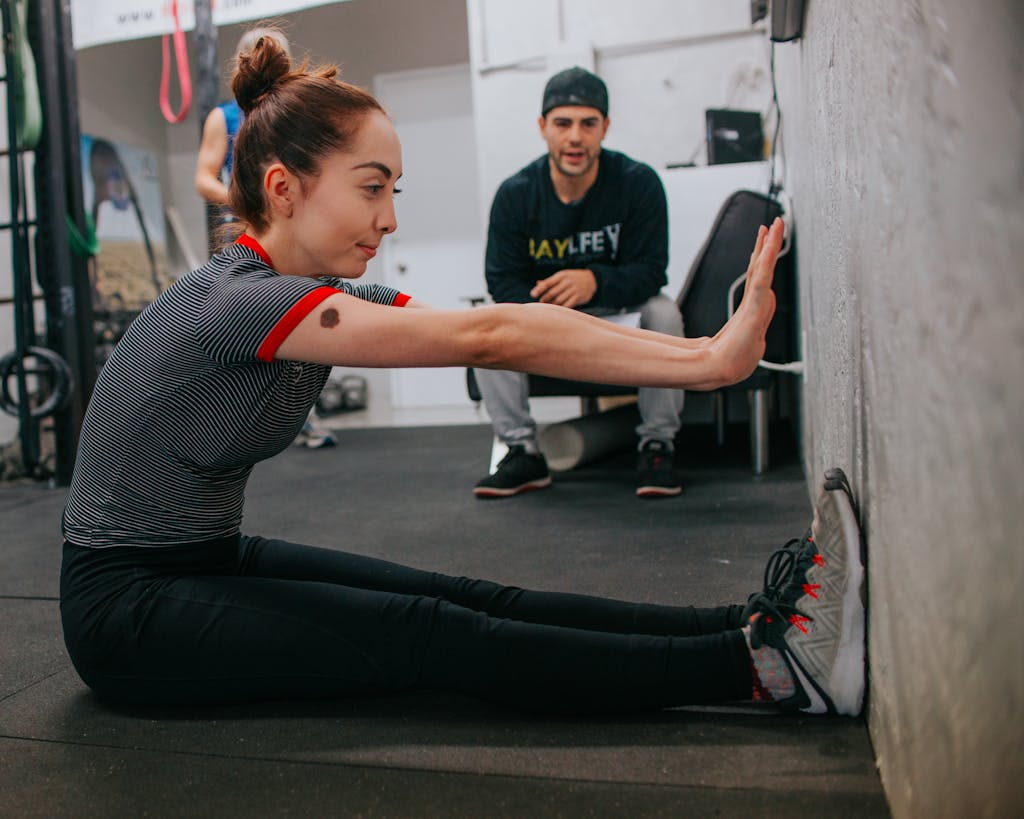 Woman stretching in a gym setting under trainer's guidance, focusing on flexibility and fitness.